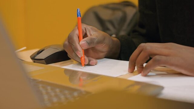 Person preparing billing details. Focused individual composing invoice notes with tools nearby. Dedicated freelancer documenting billing information using pen and computer accessories in workspace