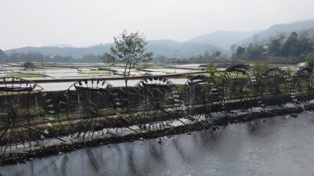 Close framing of two large bamboo water wheels at Guồng Nước N&agrave; Khương - Bản Bo turning in the current, with rice fields and rural paths behind them.