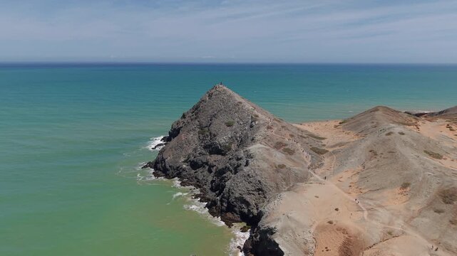 A breathtaking aerial view of Pilon de Azucar, showcasing rugged cliffs and turquoise waters under a bright blue sky, capturing the raw beauty of Cabo de la Vela from above.