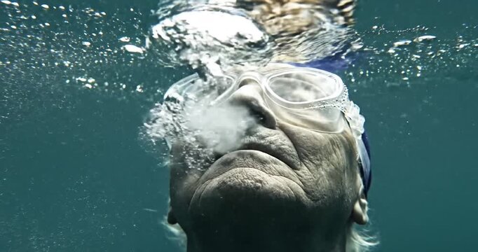 Elderly swimmer submerged in water, gazing upward with determination and serenity
