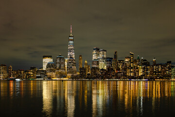 Obraz premium Lower Manhattan skyline with illuminated skyscrapers reflections. Night city skyline of Lower Manhattan. Urban New York skyline with business district towers. Famous NYC skyline.
