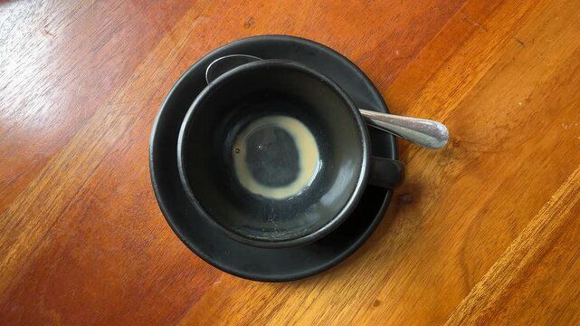 top view of empty coffee cup after drinking. black cup or mug. Glass table. Cafe, coffe shop, restaurant. Close up view. leftover, leftovers.  high angle, above, flat lay. wooden table. natural light,