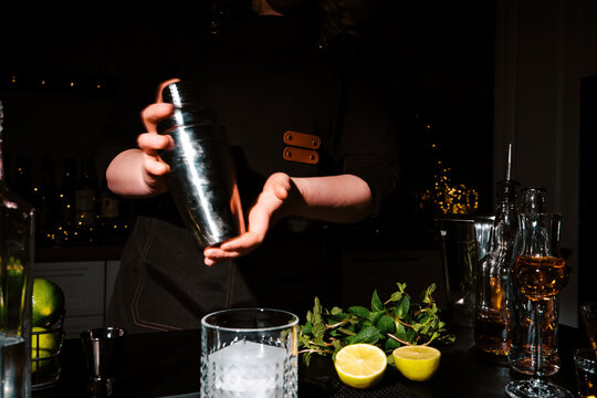 Woman bartender shaking cocktail in metal shaker with two hands. Intensive mixing process for refreshing drink and nightlife entertainment concept.