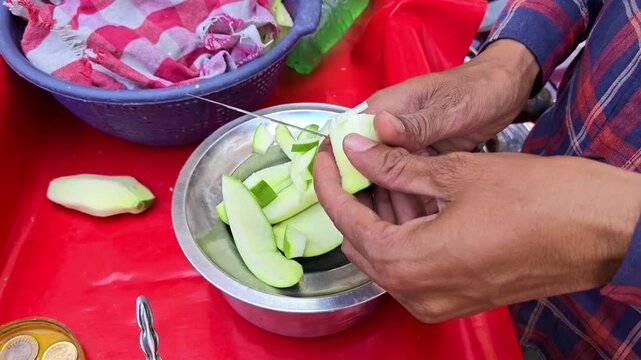 Close up of street vendor hands slicing fresh raw green mango with a knife