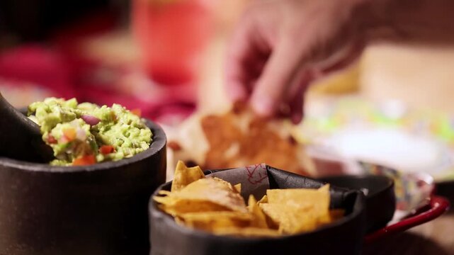 Close up of guacamole and nachos being served with a hand reaching for food.