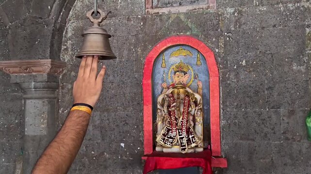 Devotee ringing brass bell in hindu temple with lord ganesha idol