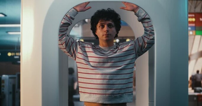 Focused Traveler Undergoes Mandatory Security Screening International Terminal. Standing With Raised Arms in Scanning Booth, Man Compliance With Strict Airport Safety Regulations. Safety Protocols.