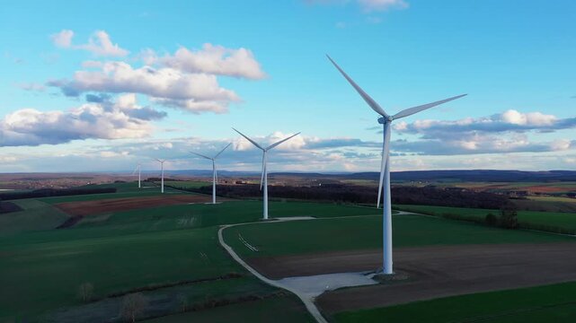 A row of modern wind turbines stands in open green fields under a blue sky with scattered clouds in the Nievre region near Oisy, France. Sustainable energy and rural landscape concept.