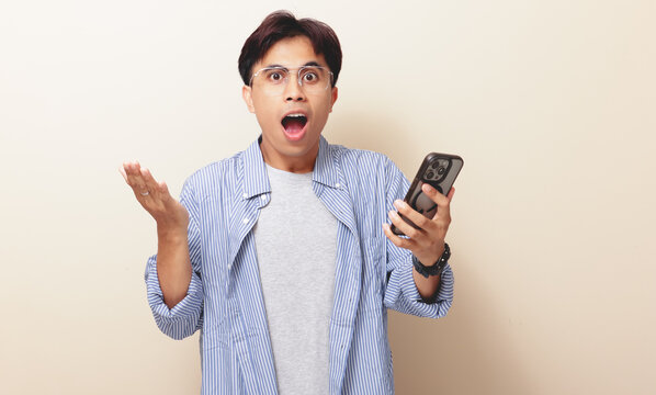 Wow face of a shocked Asian man looking at his smartphone with an amazed expression, isolated background.