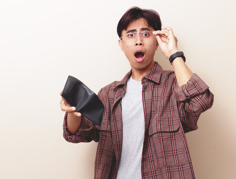 Funny shocked poor Asian man looking at empty wallet with wide open mouth expression on isolated background.