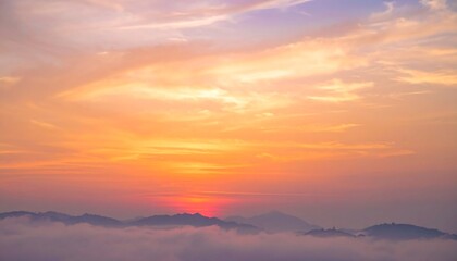 Obraz premium Vibrant sunset paints the sky with orange, purple, and pink hues. Silhouetted mountain range appears from the cloud layer below