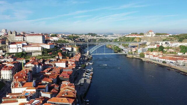 Scenic aerial shot of the Dom Luis I Bridge spanning the Douro River with the historic cityscape of Porto, Portugal under a clear blue sky.