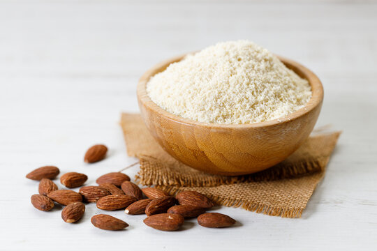 Almond meal, Almond flour, in wooden bowl with almond nuts on white table.