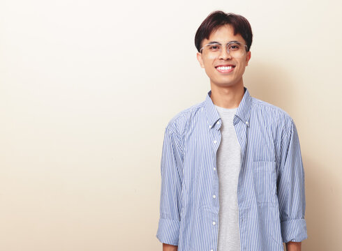 Smiling confident young Asian man standing and looking at camera on isolated background.