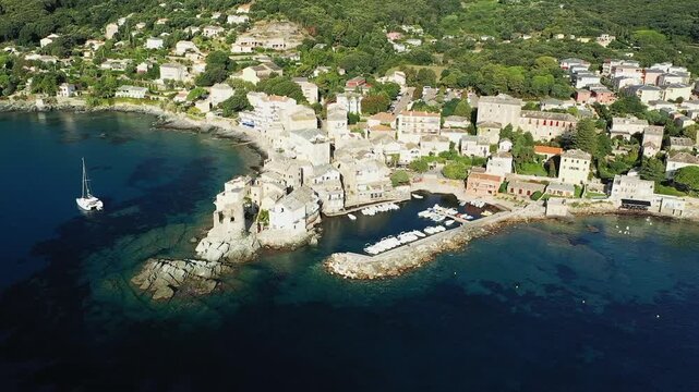 Drone shot of the picturesque Erbalunga village on the coast of Corsica, featuring traditional stone buildings, a small harbor, and clear blue Mediterranean waters.