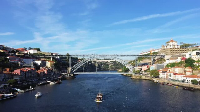 Wide view of the iconic Dom Luis I Bridge spanning the Douro River in Porto, Portugal, with historic cityscape and blue sky.