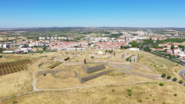Drone shot of the historic Forte de Santa Luzia fortress surrounded by the cityscape and countryside of Elvas, Portugal, on a clear sunny day.