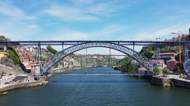 Wide view of the iconic Dom Luis I Bridge spanning the Douro River in Porto, Portugal, with colorful buildings and clear blue sky.
