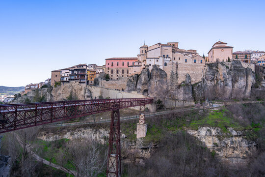 A scenic view of the iconic red iron San Pablo Bridge spanning the Huecar Gorge, connecting the historic city of Cuenca to the San Pablo Convent.