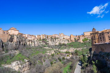 Fototapeta premium A panoramic view of the historic city of Cuenca, Spain, featuring ancient buildings perched on dramatic limestone cliffs above a deep river gorge.