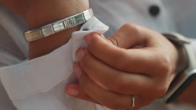 Hands adjusting cuff bracelet closeup, woman smoothing linen sleeve with manicured fingers, silver bangle catching warm sunlight, ring on finger, calm poised mood, everyday style detail for fashion