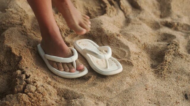 Bare feet slipping out of white sandals on warm sand. Closeup sequence of a beachgoer removing flipflops, scattering grains, and leaving paired sandals behind playful, freeing mood with twilight hues