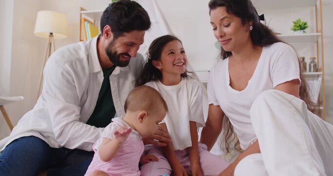 Happy family with parents, children, baby, toddler play blocks. Parents encourage stacking and problem solving at home, while girl smiles and baby explores educational shapes. Leisure and learning.