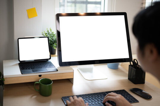 Shoulder to back view. young man using computer and tablet at workplace close up view of white screen. mock up banner for website header design with copy space for text