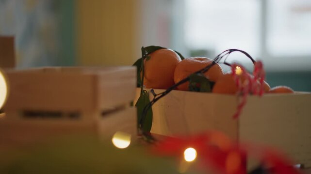 Box of oranges with fairy lights, rustic crate filled with citrus and ribbon, candy pieces and twine peeking out, soft bokeh window light, warm kitchen setting, festive present composition