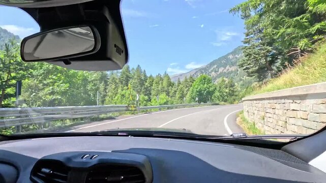 A dynamic first person perspective of driving through scenic mountain roads with lush green trees and other cars on a clear sunny day.