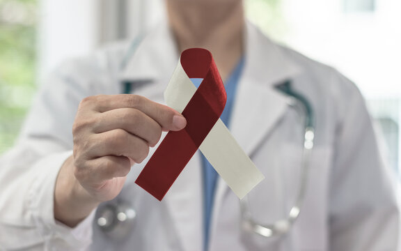 Burgundy ivory ribbon awareness on doctor's hand, symbolic bow color for head and neck cancers, oral squamous cell carcinoma, throat, laryngeal and pharyngeal cancer