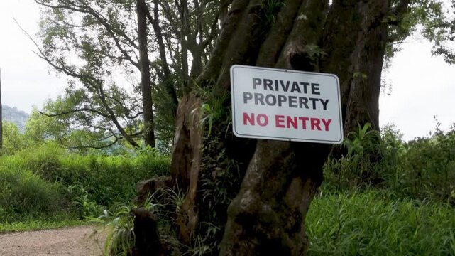 Private property no entry sign posted on old mossy tree in lush tropical forest environment during daylight.