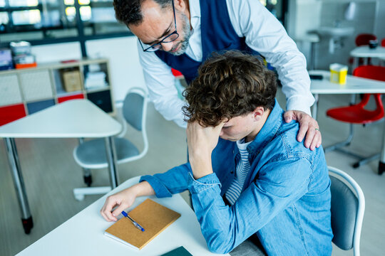 Teacher supporting struggling student with learning difficulties during lesson.