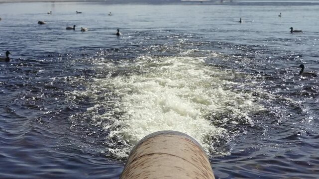 Dirty water discharging from a large industrial drainpipe into a lake, creating foam and turbulence while ducks swim in the contaminated environment, highlighting environmental pollution