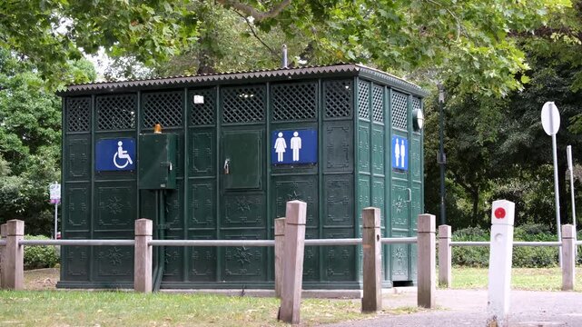 Ornate dark green cast iron public toilet amenities block in a Melbourne park in Australia, featuring disability wheelchair access symbol, male and female gender symbols, and unisex signage. 