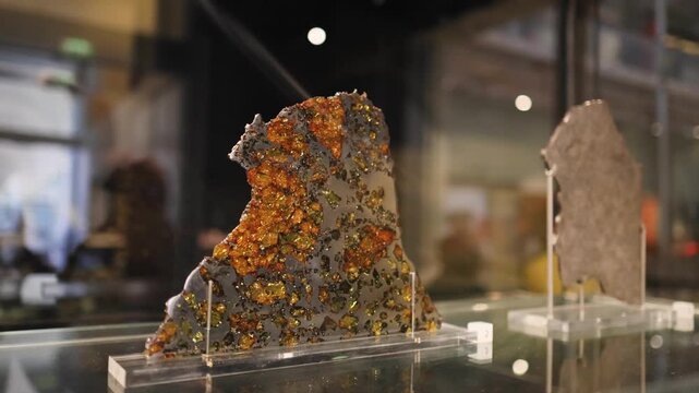 Close up of meteorite section with orange crystals in museum exhibit.