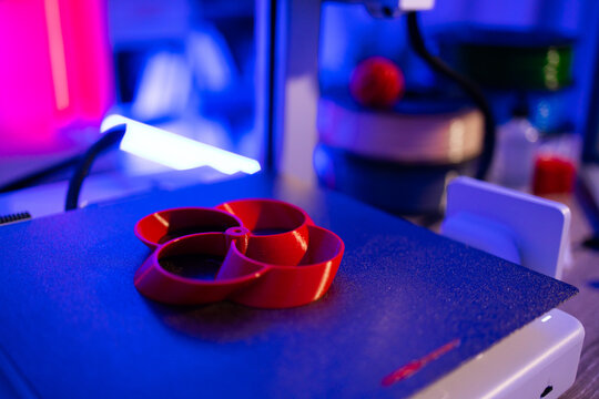 A red 3D printed object is being created on a 3D printer with blue and pink lighting