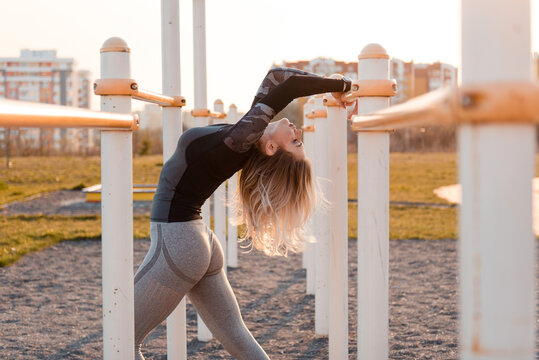 Woman stretching her back on outdoor gym equipment at sunset
