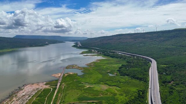 Aerial view of highway running along river and green hills. Transportation, infrastructure, travel and logistics concept
