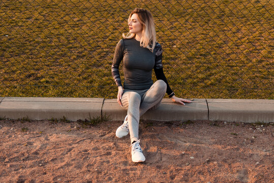 Woman in athletic wear relaxing by a fence during golden hour