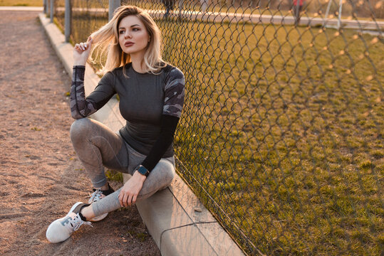Woman in athletic wear resting by a fence after a workout session