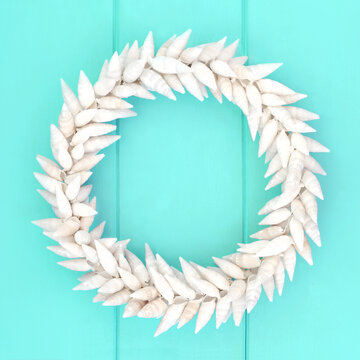 Spindle white seashell natural wreath on rustic turquoise wood background. Round shape garland decoration symbol of summer seaside.