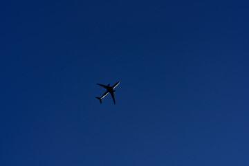 Fototapeta premium Passenger airplane flying overhead against deep blue sky, minimal composition in spring or summer with sense of freedom and motion.