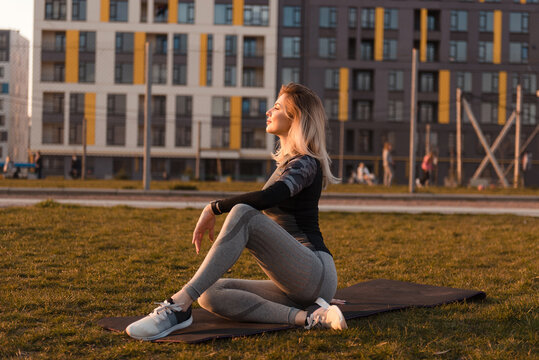 Woman stretching on yoga mat outdoors with modern buildings in background