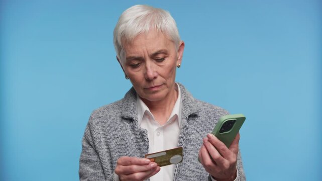 Senior woman paying online with smartphone on blue