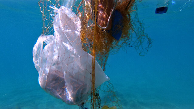 Fishing net with plastic bag underwater, showing pollution and environmental damage. The clear blue water contrasts with the dirty plastic, emphasizing the impact of human waste on marine ecosystems.