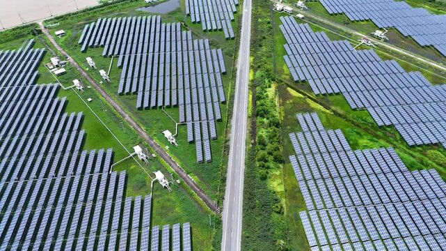 High-angle drone footage capturing large solar panel arrays beside a rural road and farmland, illustrating clean energy production, sustainable infrastructure, and modern renewable power generation