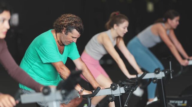 Diligent middle-aged man doing spin bike exercises in well-equipped gym during training session