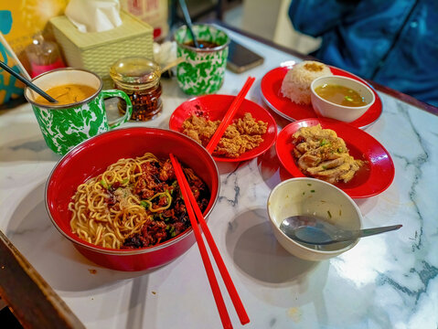 Various Malaysian kopitiam dishes featuring wonton mee noodles, crispy fried chicken, steamed chicken, and classic enamel mugs on a marble table.