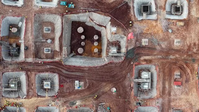 Aerial view of a construction site in progress. Workers move around the freshly dug foundations